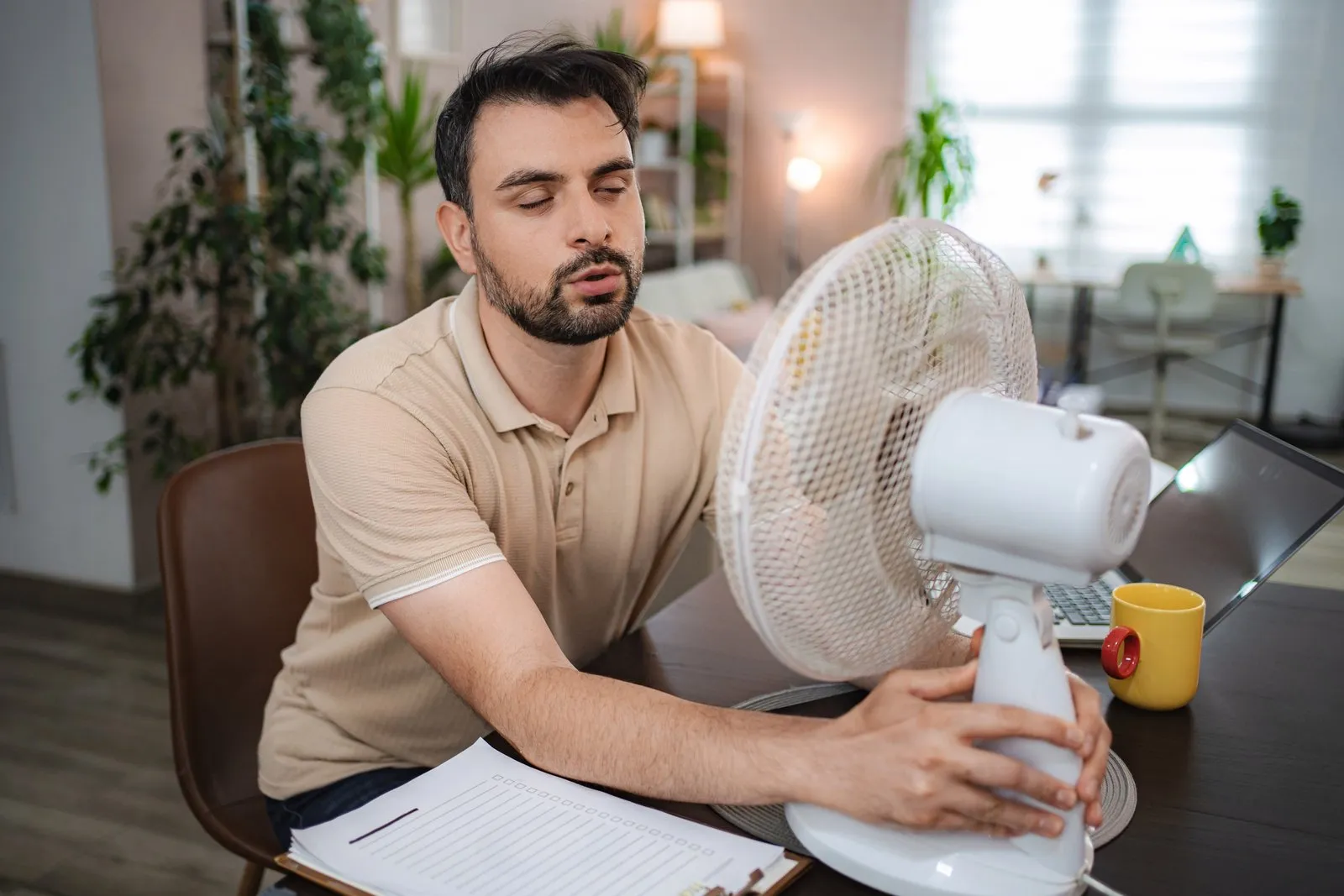 Illustrative stock photo — a man working from home cools himself with a desk fan during a heat wave; not an actual Lake Havasu AC Guide job site.